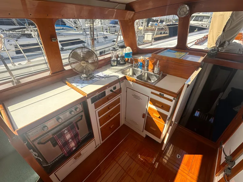 Slide: The Image of 1969 Calkins 50 Pilot House kitchen with wood finish, stove, sink, and marina view. - 26