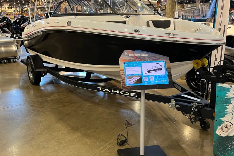 Slide: The Image of 2024 Tahoe 200 S boat on display with informational stand in showroom. - 0