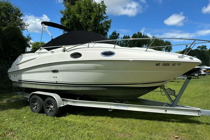 The Image of 2007 Sea Ray 240 Sundancer boat on trailer, parked on grass under blue sky. - 0