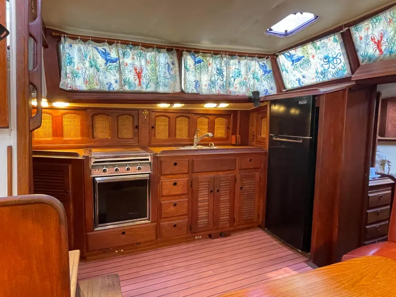 Slide: The Image of 1978 Islander Freeport 41 Ketch interior kitchen with wood cabinetry and nautical curtains. - 42