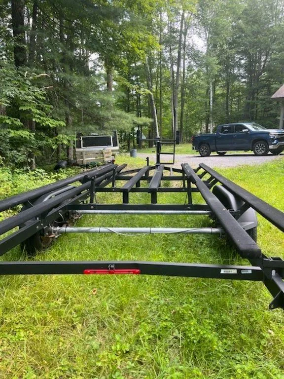 Slide: The Image of 2020 Regency 230 DL3 boat trailer on grassy area with trees and vehicles in the background. - 42