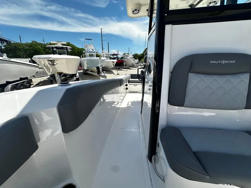 Slide: The Image of 2024 NauticStar 242 OSL boat interior with gray seating, docked under a blue sky. - 12