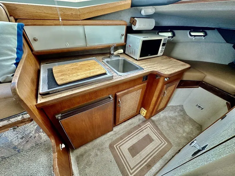Slide: The Image of 1986 Bayliner 2850 Command Bridge interior kitchen with sink, microwave, and wooden cabinetry. - 19