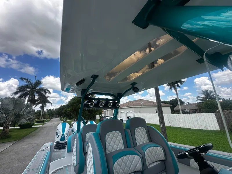 Slide: The Image of 2021 Renegade 38 Open boat interior with teal and white seating, under a clear blue sky. - 11