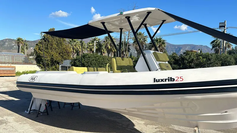 Slide: The Image of Aqvaboats Luxrib 25, 2025 model, sleek design with canopy, parked outdoors. - 1