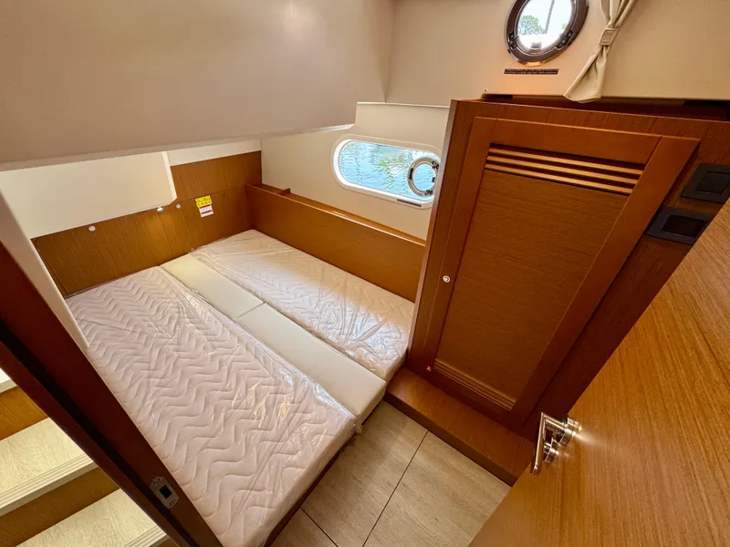 Slide: The Image of 2025 Beneteau Swift Trawler 41 Fly cabin with bed, wooden interior, and porthole window. - 10