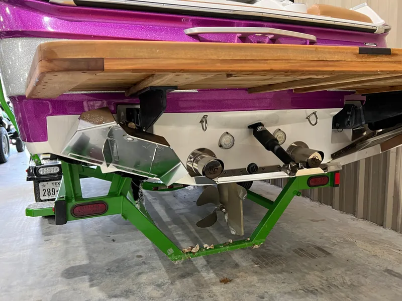 Slide: The Image of 2016 MasterCraft X26 boat with vibrant purple and green accents, rear view in storage. - 12