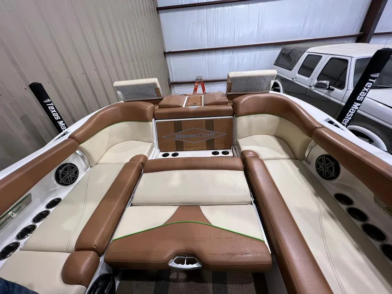 Slide: The Image of 2016 MasterCraft X26 boat interior with tan and cream seating, cup holders, and speakers. - 18