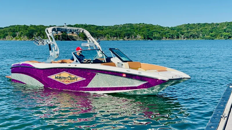 Slide: The Image of 2016 MasterCraft X26 boat on a lake with lush green shoreline. - 2