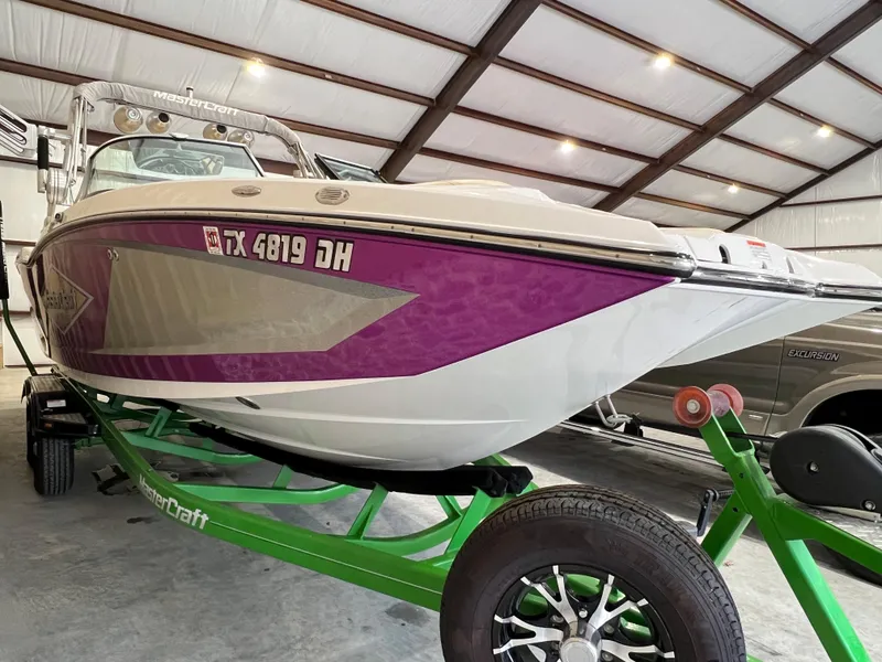 Slide: The Image of 2016 MasterCraft X26 boat with purple accents on a green trailer in a garage. - 7