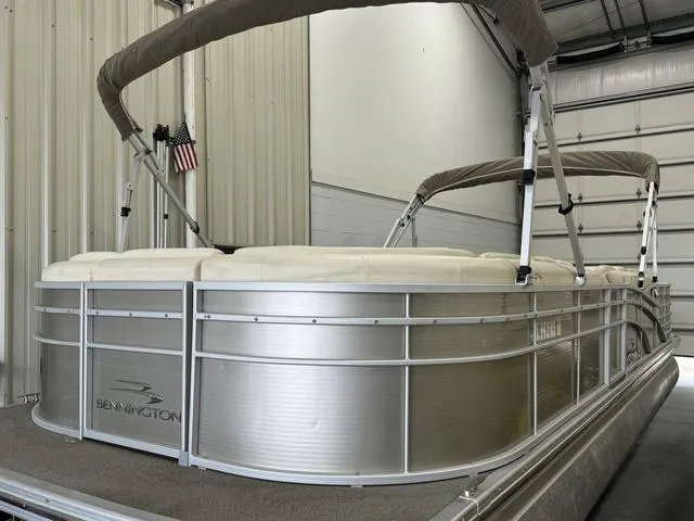Slide: The Image of 2013 Bennington 2575 R pontoon boat in storage, featuring beige canopy and sleek design. - 3