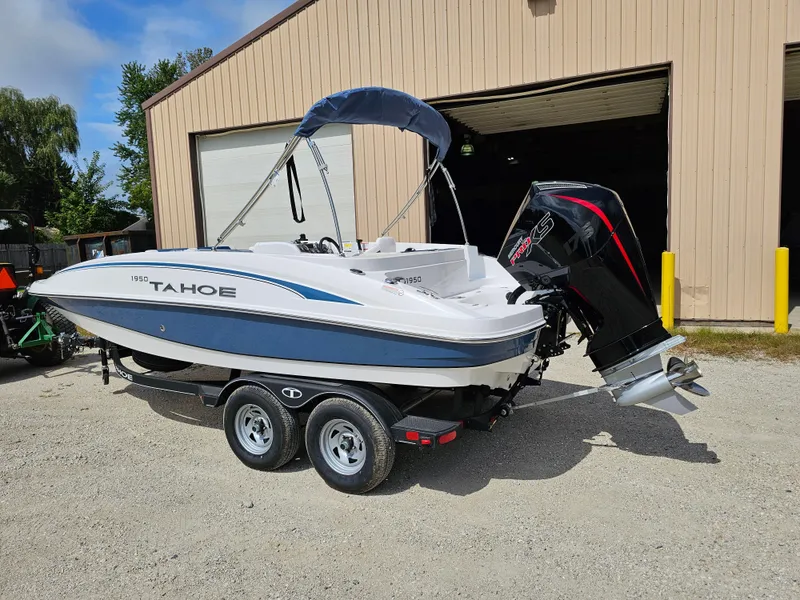 Slide: The Image of 2024 Tahoe 1950 boat with outboard motor on trailer, parked outside a garage. - 1