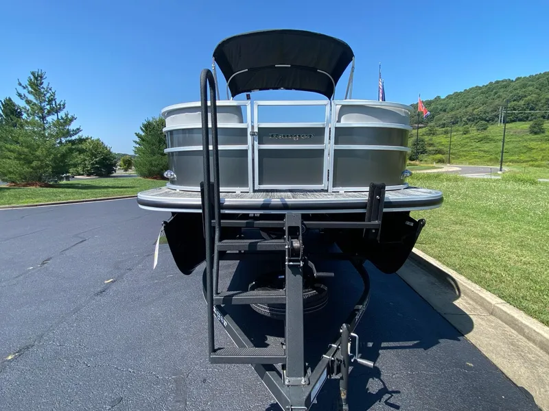 Slide: The Image of 2024 Ranger Reata 223C pontoon boat on trailer, parked on asphalt, with scenic background. - 3