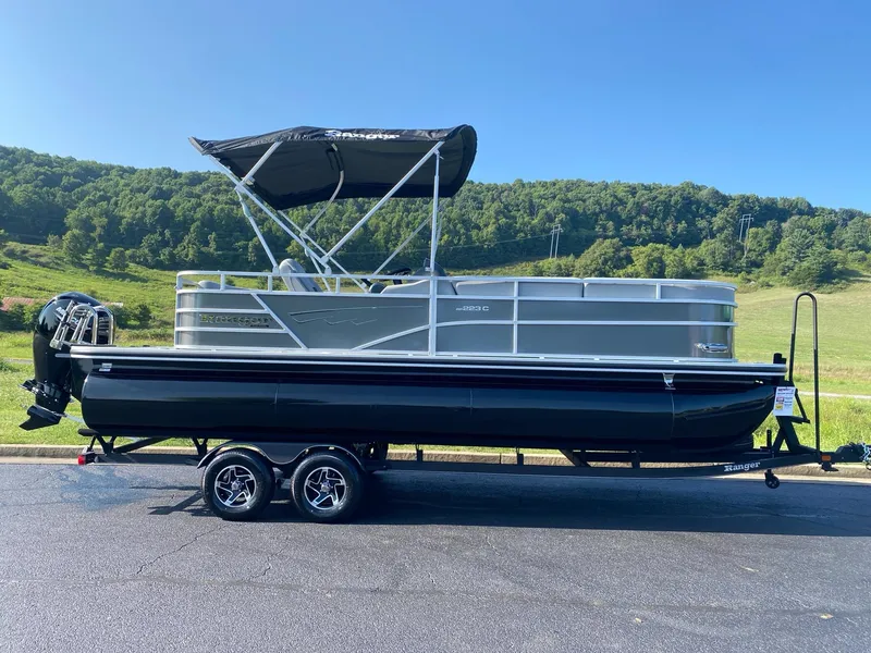 The Image of 2024 Ranger Reata 223C pontoon boat with canopy on trailer, scenic background. - 0