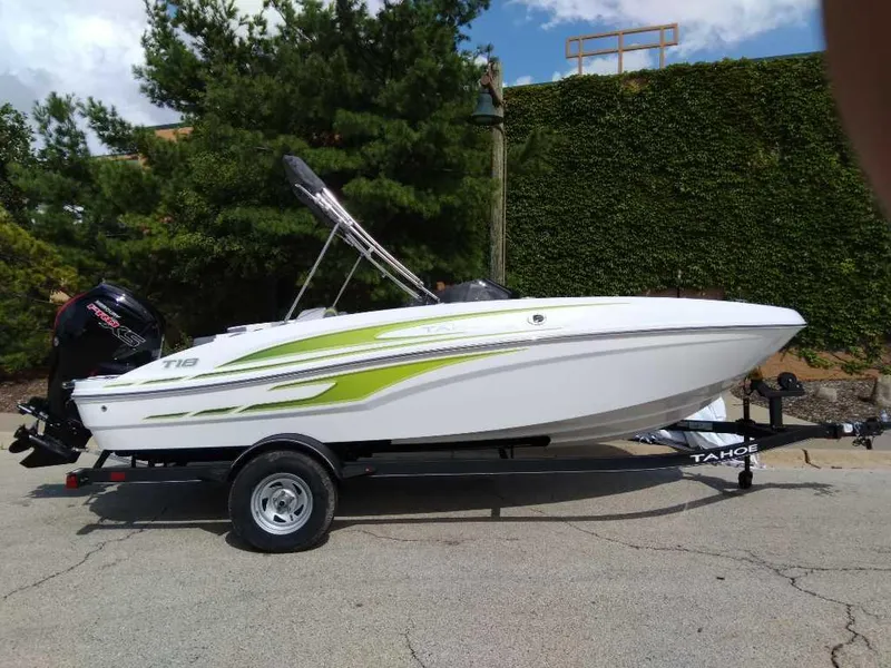 Slide: The Image of 2024 Tahoe T18 boat on trailer, white with green accents, parked outdoors. - 0