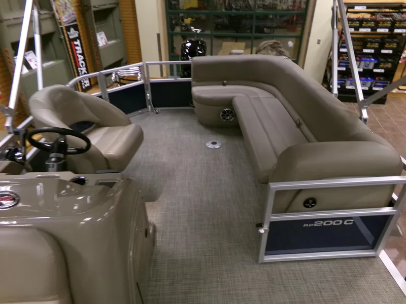 Slide: The Image of 2024 Ranger Reata 200C pontoon boat interior with beige seating and steering console. - 2