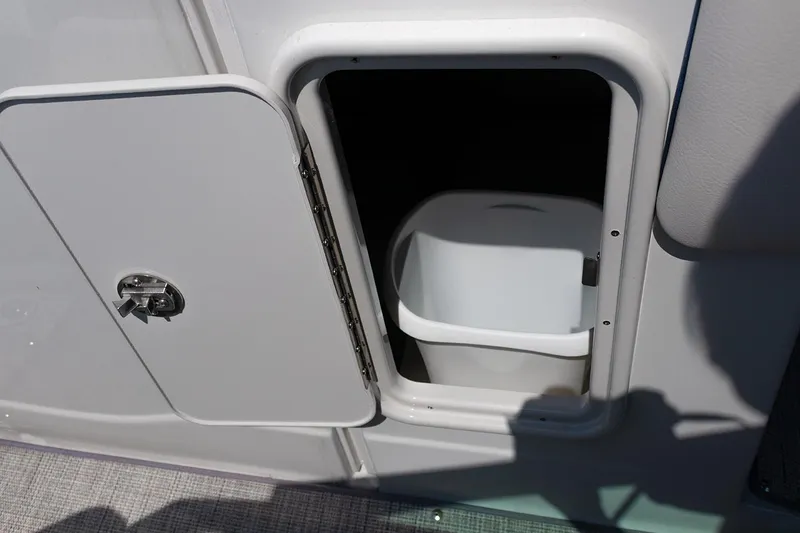 Slide: The Image of 2022 Crownline E 255 XS boat storage compartment with open door and white container. - 9