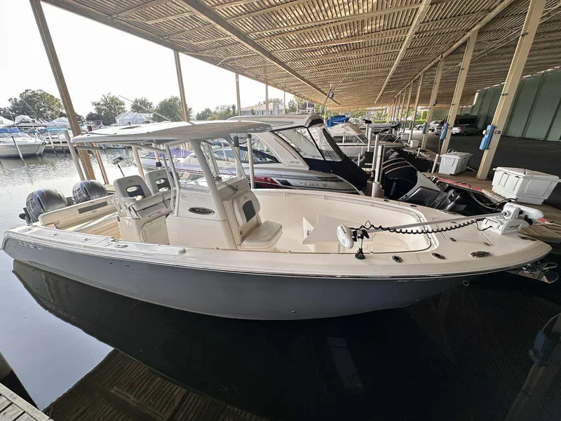 The Image of 2022 Cobia 280 Center Console boat docked in marina under covered shelter. - 0