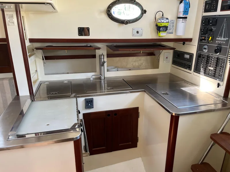 Slide: The Image of Compact kitchen area in a 2016 Alajuela 38 sailboat, featuring stainless steel countertops and wooden cabinets. - 46