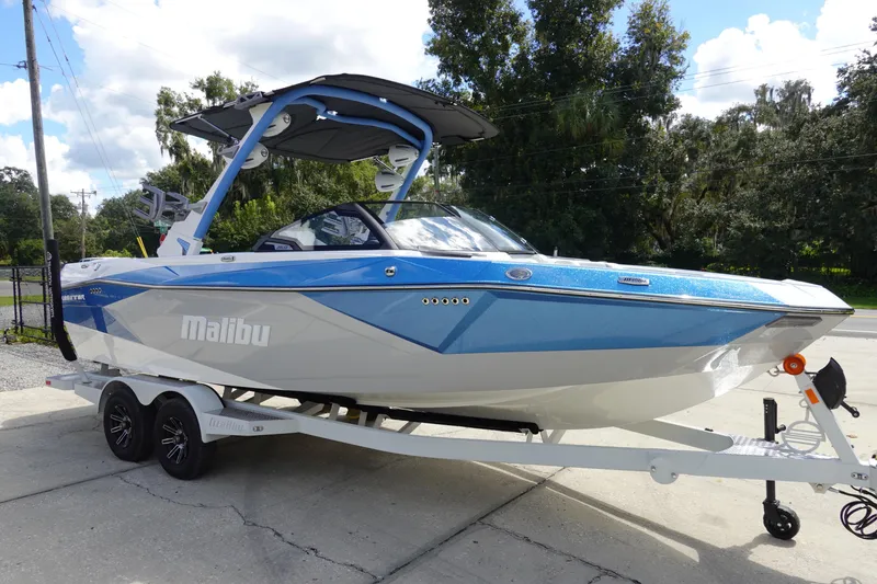 Slide: The Image of 2025 Malibu 23 LSV WAKESETTER boat on trailer, blue and white design, parked outdoors. - 4