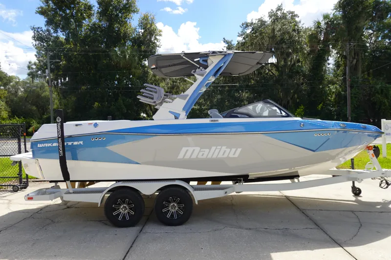 Slide: The Image of 2025 Malibu 23 LSV WAKESETTER boat on trailer, blue and white design, parked outdoors. - 5