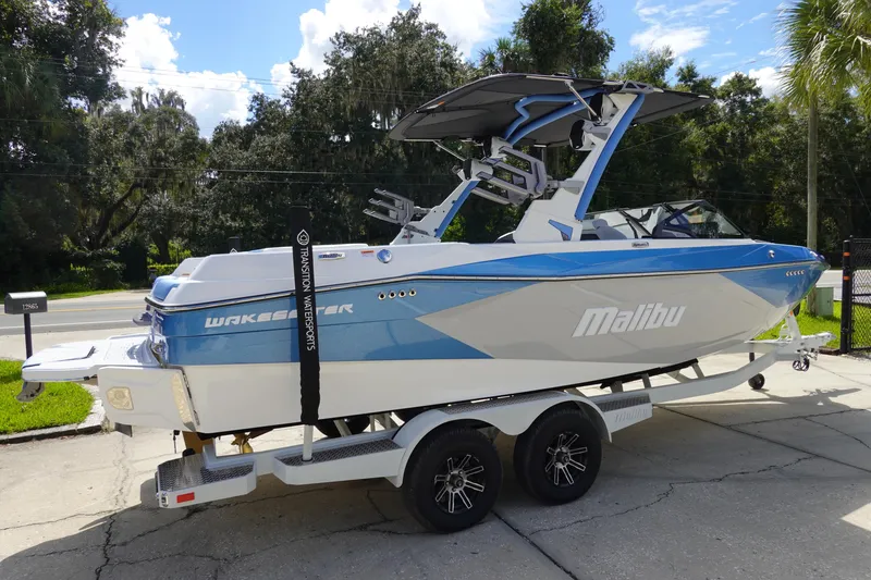 Slide: The Image of 2025 Malibu 23 LSV WAKESETTER boat on trailer, blue and white design, parked outdoors. - 6