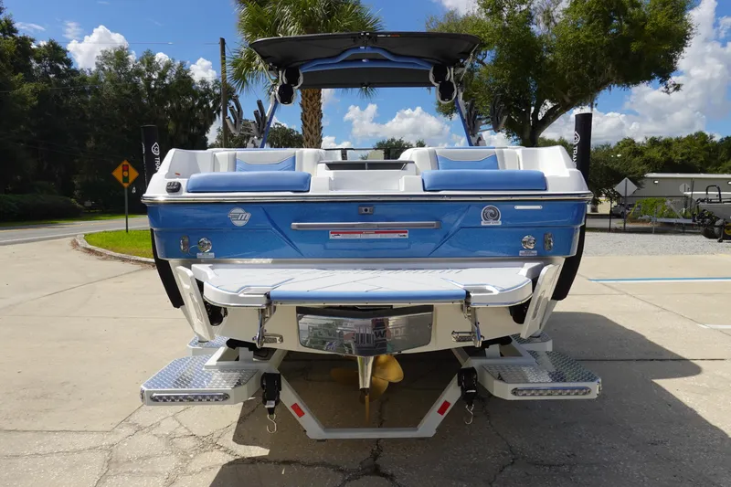 Slide: The Image of 2025 Malibu 23 LSV WAKESETTER boat, rear view, blue and white design, parked outdoors. - 7