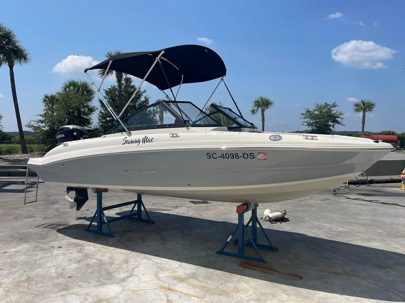 The Image of 2021 Stingray 191 DC boat on stands, with canopy, outdoors under blue sky. - 0