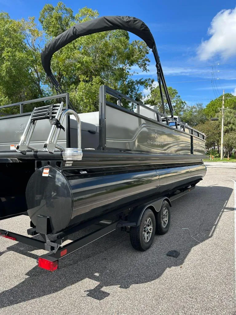 Slide: The Image of 2024 Regency 250 DL3 pontoon boat on trailer, parked outdoors. - 8