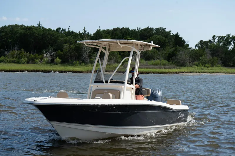 The Image of 2025 Scout 195 Sportfish boat cruising on a calm river with lush green shoreline. - 0