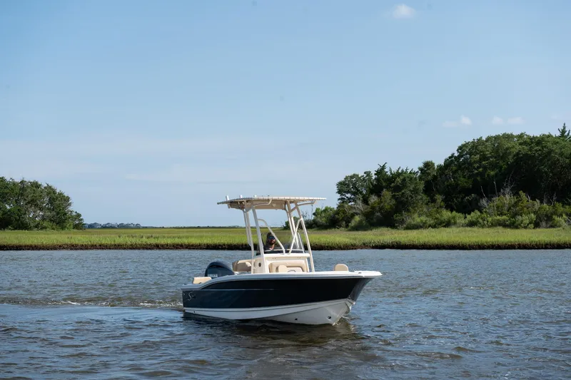 Slide: The Image of 2025 Scout 195 Sportfish boat cruising on a calm river with lush green shoreline. - 2
