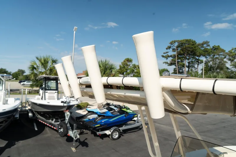 Slide: The Image of 2025 Scout 195 Sportfish boat with rod holders, parked near other boats and jet skis. - 29