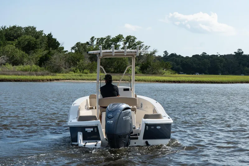 Slide: The Image of 2025 Scout 195 Sportfish boat cruising on a calm river with lush greenery. - 4