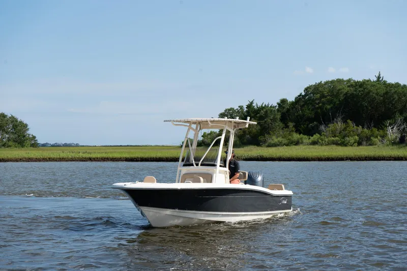 Slide: The Image of 2025 Scout 195 Sportfish boat cruising on a calm river with lush green shoreline. - 5