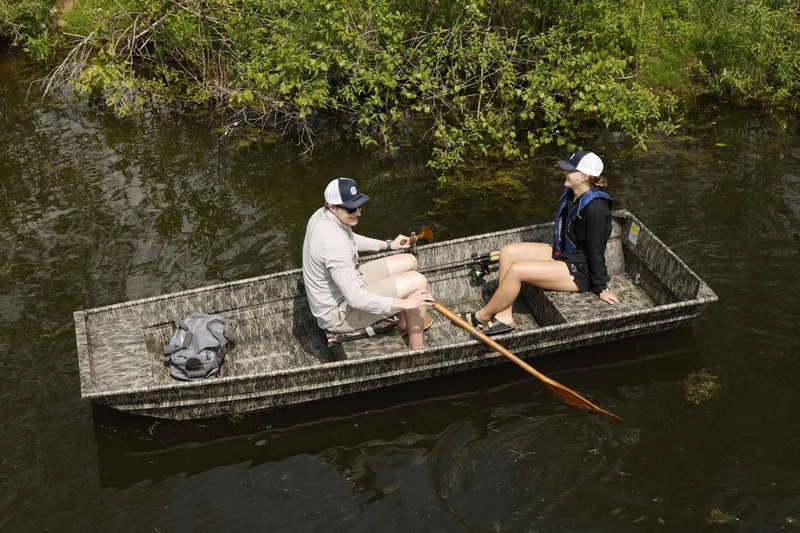 Slide: The Image of Two people in a 2025 Starcraft 1436 JON TS boat on a calm river. - 1
