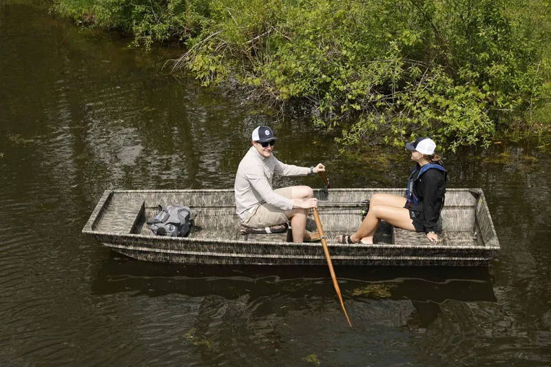 Slide: The Image of Two people in a 2025 Starcraft 1436 JON TS boat on a calm river. - 2