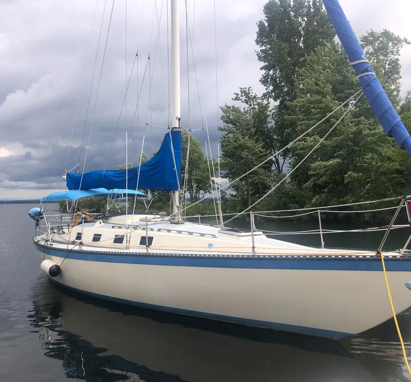 The Image of 1980 Lancer 36 sailboat with blue trim docked on a calm lake. - 0
