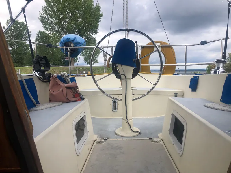 Slide: The Image of 1980 Lancer 36 sailboat cockpit with steering wheel, blue seating, and overcast sky. - 20