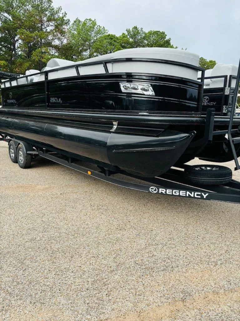 Slide: The Image of 2024 Regency 250 LE3 pontoon boat on trailer, black exterior, parked outdoors. - 2