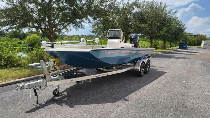 The Image of 2024 Ranger RB200 boat on trailer, parked outdoors, surrounded by trees and blue sky. - 0
