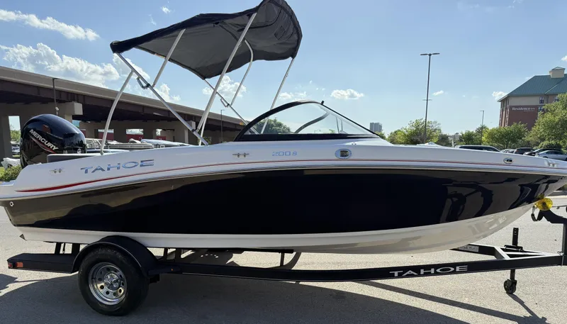 Slide: The Image of 2024 Tahoe 200 S boat with canopy on trailer, parked outdoors under clear sky. - 2