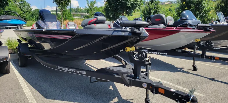 Slide: The Image of 2024 Ranger RT188 boat on trailer in parking lot, surrounded by trees and other boats. - 2