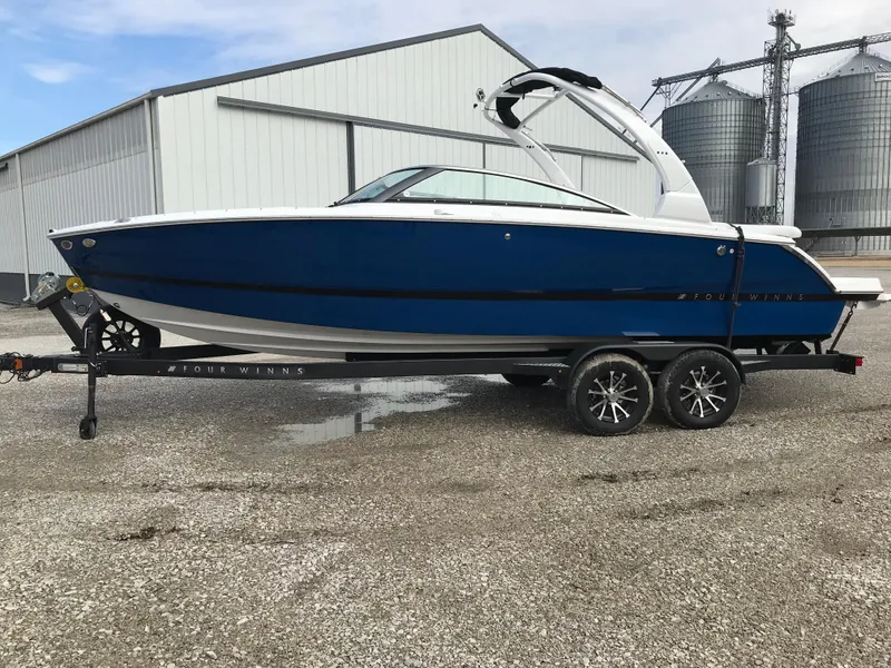 The Image of 2025 Four Winns H4 boat on trailer, blue and white design, parked outdoors. - 0