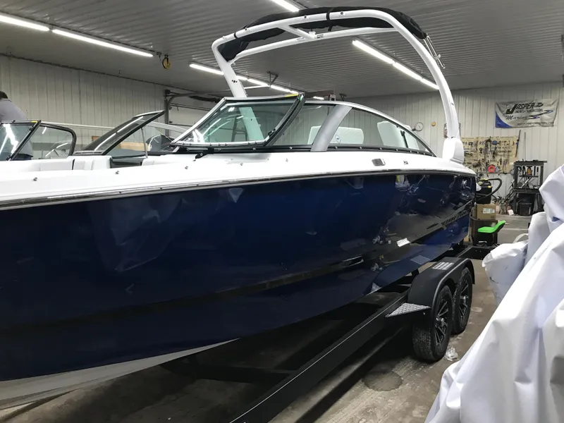 Slide: The Image of 2025 Four Winns H4 boat in showroom, blue hull, on trailer. - 2