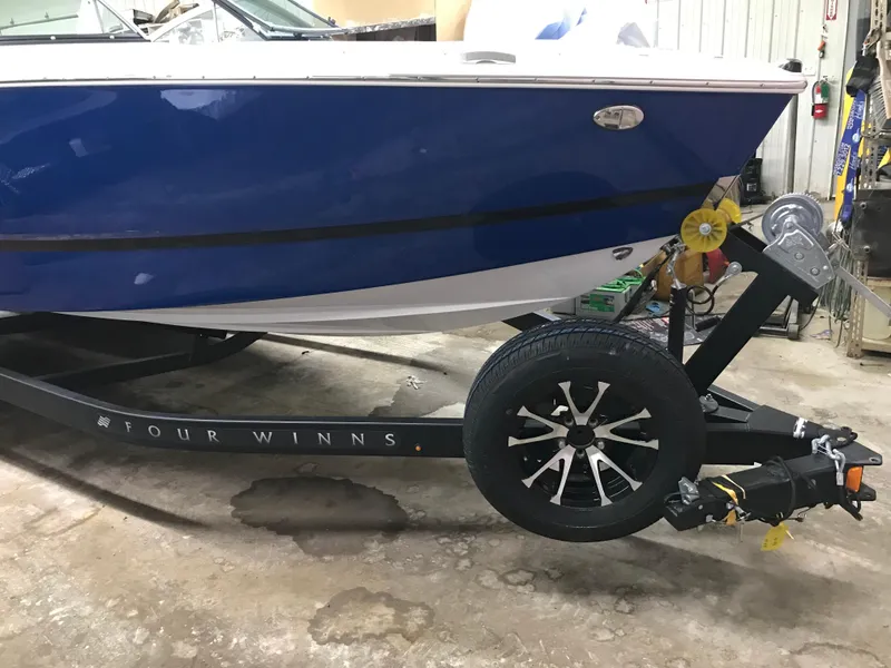 Slide: The Image of 2025 Four Winns H4 boat on trailer, blue hull, black wheel, indoor setting. - 6