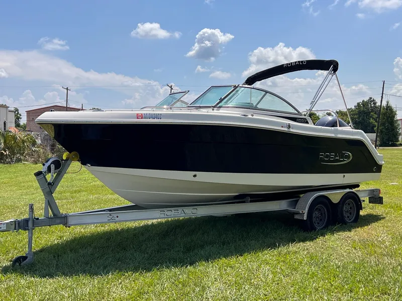 Slide: The Image of 2021 Robalo R227 Dual Console boat on trailer, parked on grass under blue sky. - 1
