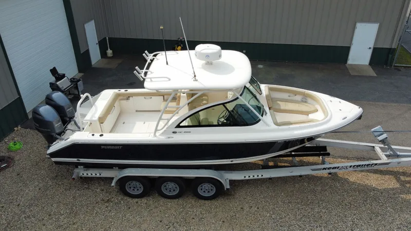 Slide: The Image of 2016 Pursuit DC 265 Dual Console boat on trailer, parked outside a building. - 2
