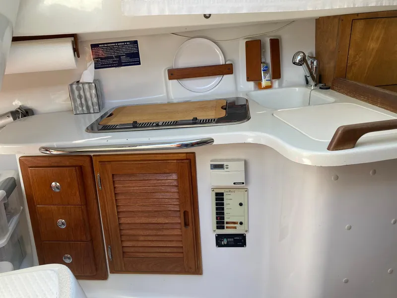 Slide: The Image of Interior of a 2006 Hake Seaward 26RK sailboat, featuring a compact kitchen area with wooden cabinetry. - 6