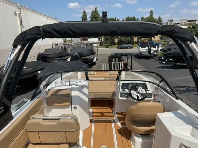 Slide: The Image of 2025 Bayliner D22I boat interior with tan seating and modern dashboard, parked outdoors. - 11