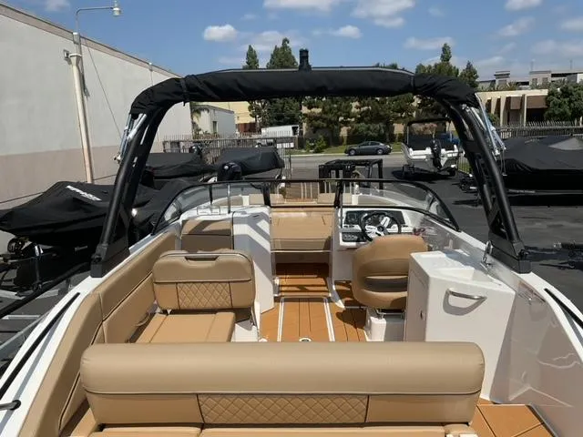 Slide: The Image of 2025 Bayliner D22I boat interior with tan seating and modern dashboard, parked outdoors. - 9